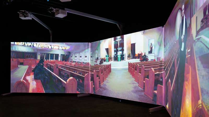 A church interior is projected across curved screens in the Community Safety Simulation Center, depicting pews, an altar, and virtual individuals in a faith-based scenario for safety training.