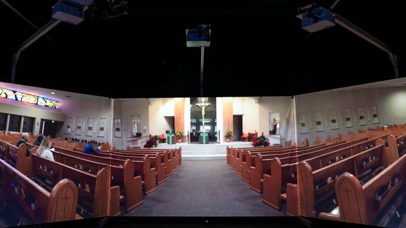 A church interior is projected across curved screens in the Community Safety Simulation Center, depicting pews, an altar, and virtual individuals in a faith-based scenario for safety training.