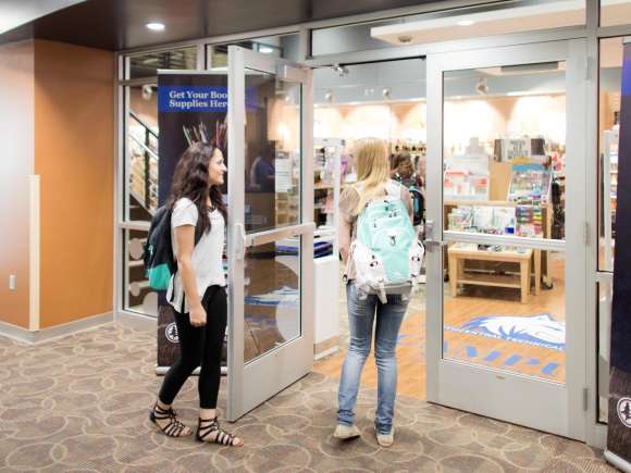 Two female students chat as they open the door to the campus store, before heading inside.