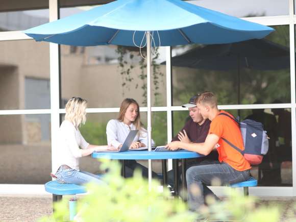 Four students sitting at a picnic table in the courtyard of the Wausau campus.