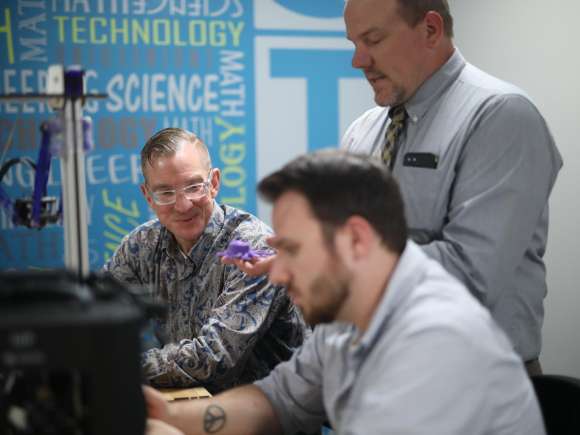 Two students, seated, listen to instructor explaining something.