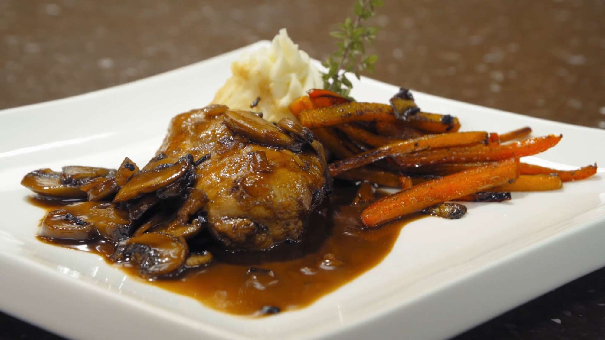 A finely arranged plate with chicken in a mushroom sauce, roasted carrots, and mashed potatoes.
