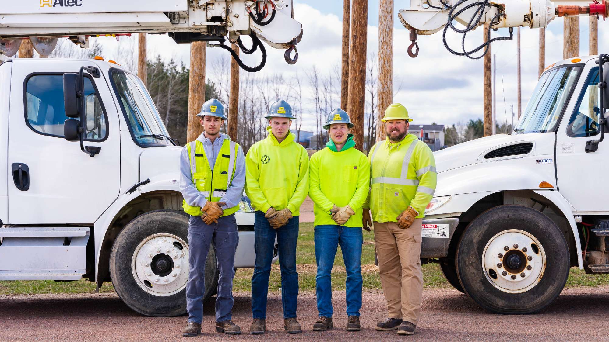 Electrical Power Distribution program students and instructor pose in their work gear in front of two trucks.