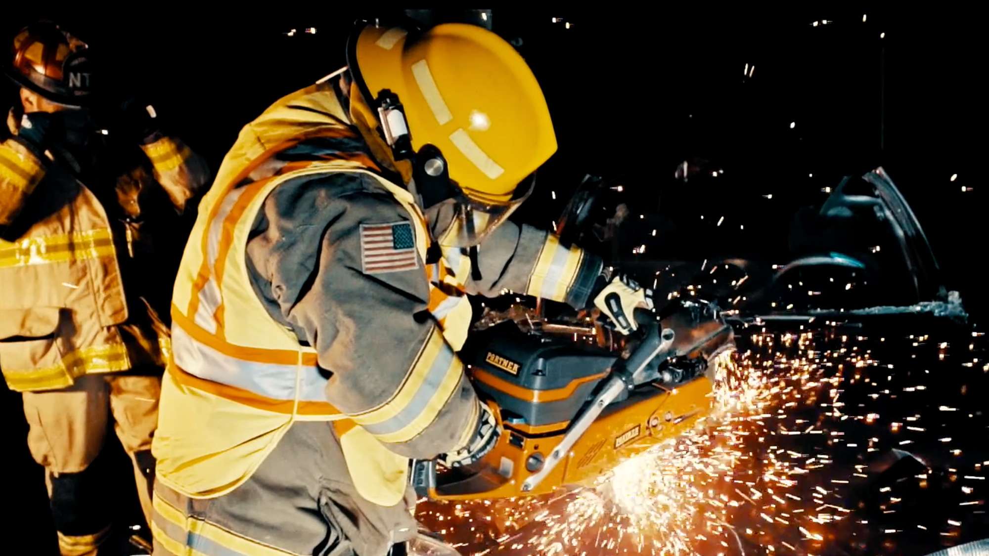 Firefighter uses a power saw to cut a vehicle at night as sparks fly during extrication training.
