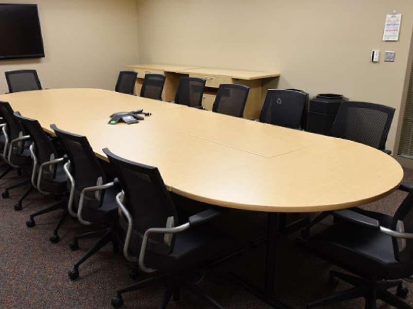 A conference room with one table lined by conference chairs on each side and at the ends.