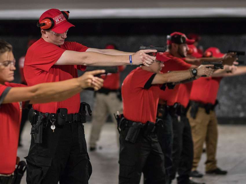 Campus security recruits are doing a training drill at a firing range. They're aiming their firearms at a target