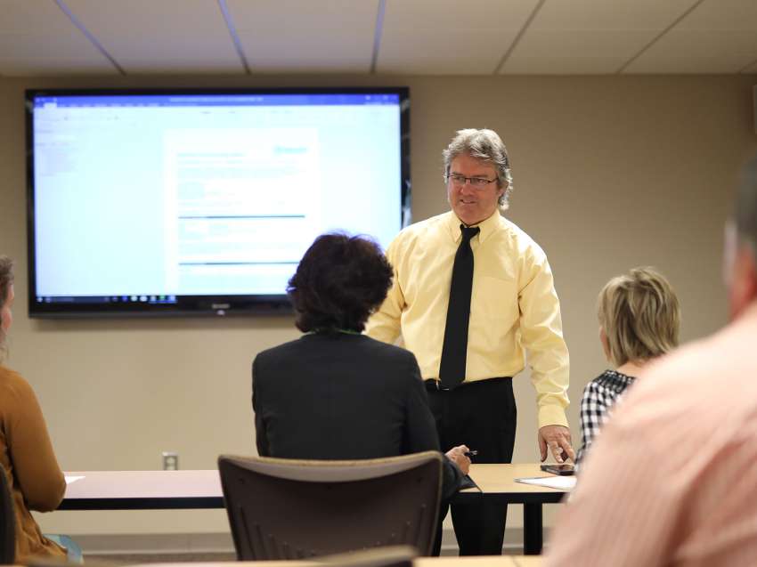 A businessman is standing up in front of a room full of businesspeople giving a lecture