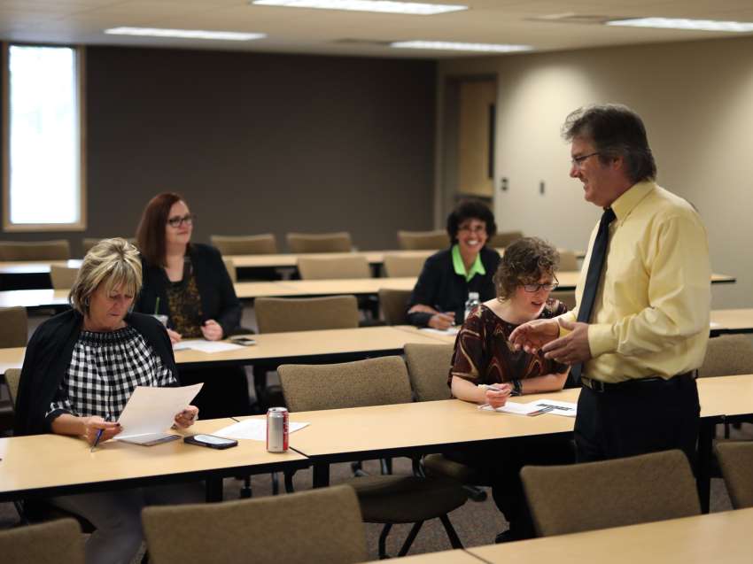 A businessman running a customized training session with several other professionals in attendance, seated at desks.