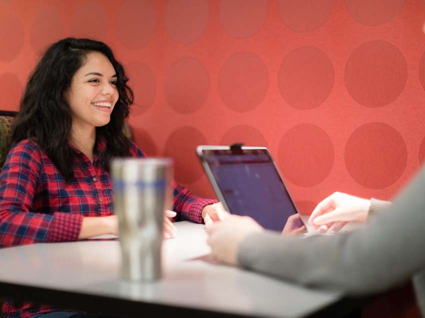 A student sits in a booth near the Campus Cafe, across from another individual, who is in the foreground, just off camera.
