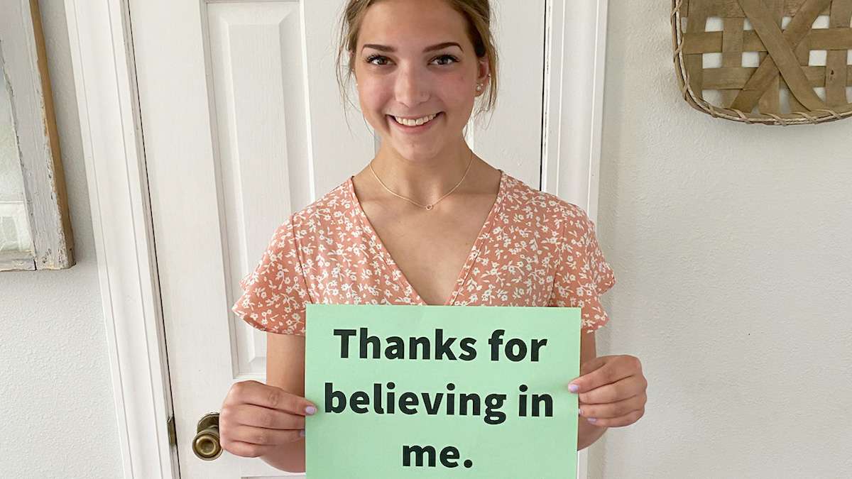 An NTC student holds up a small sign with "Thanks for believing in me" written on it.