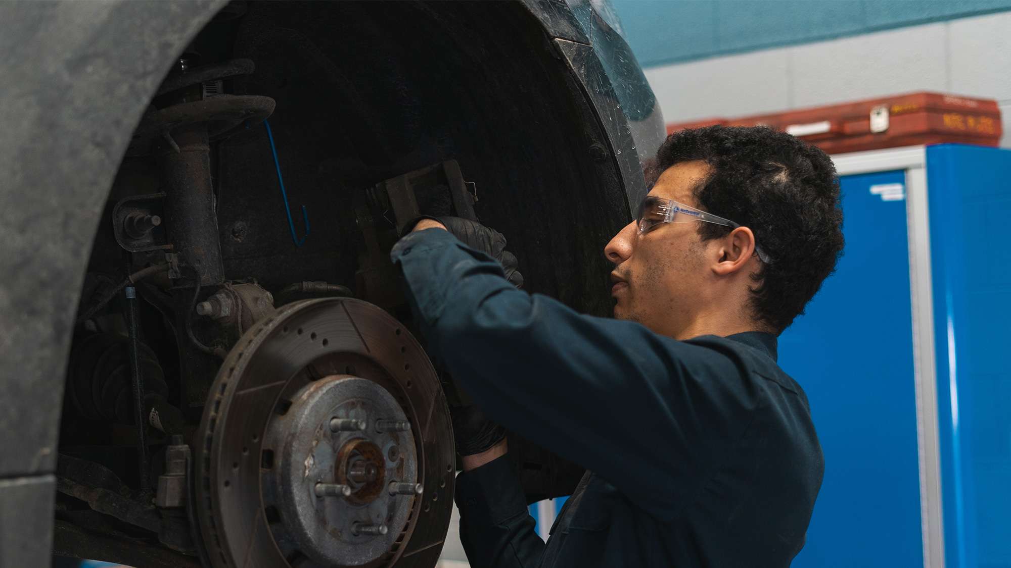 An automotive technician is working on the wheel of a vehicle suspended in the air inside of a maintenance garage.