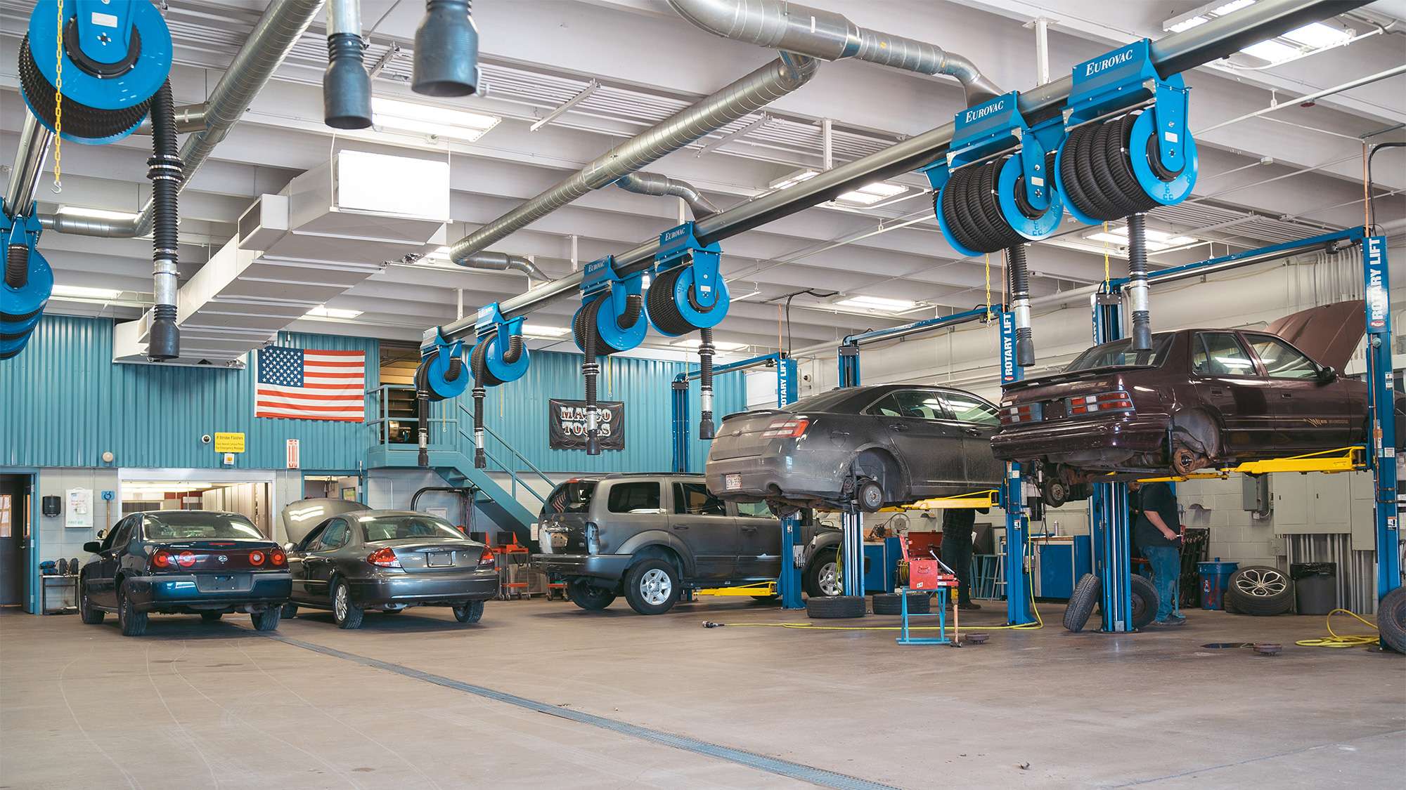 Wide interior view of NTC's automotive repair shop with several vehicles being worked on by student automotive technicians.