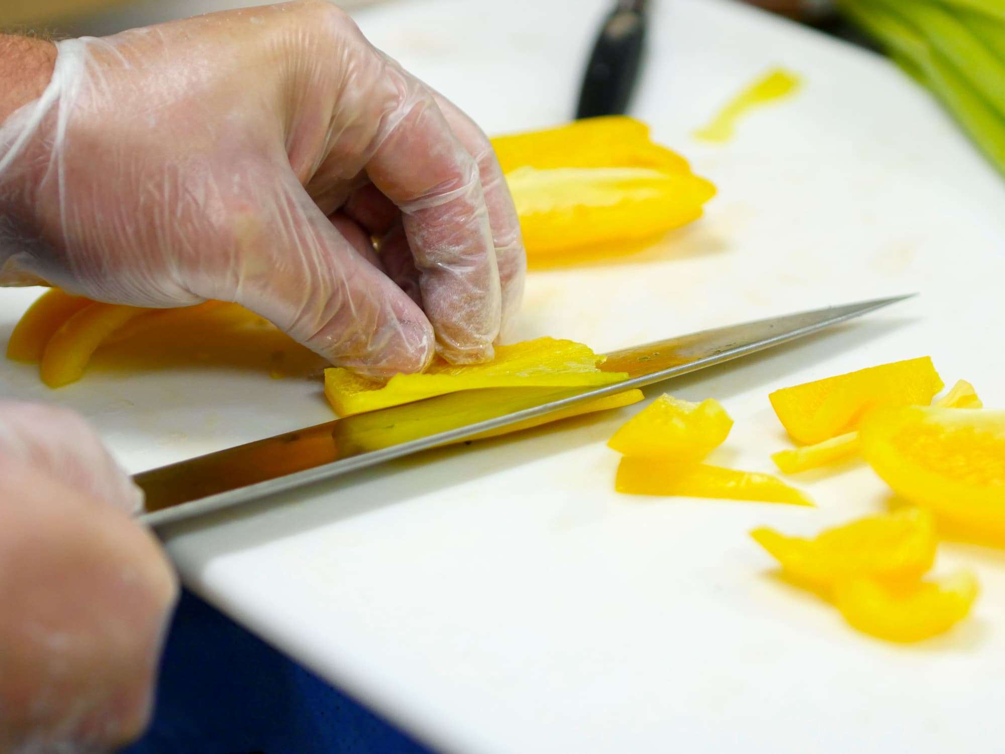 A close-up of a student slicing a yellow pepper into razor-thin pieces.