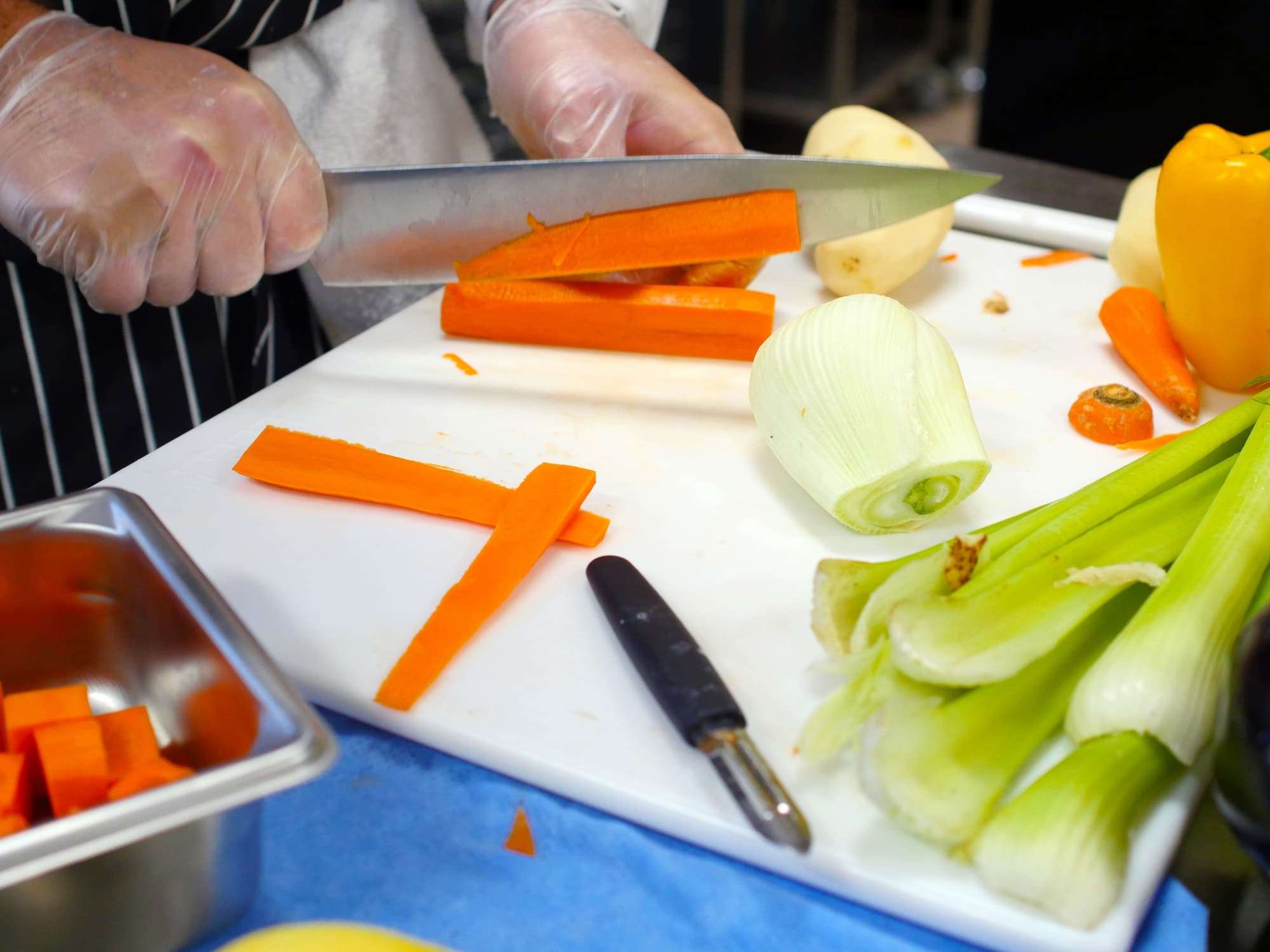 A close-up of a variety of vegetables being prepared: sliced carrots, celery, peeled potatoes, and a sweet pepper.
