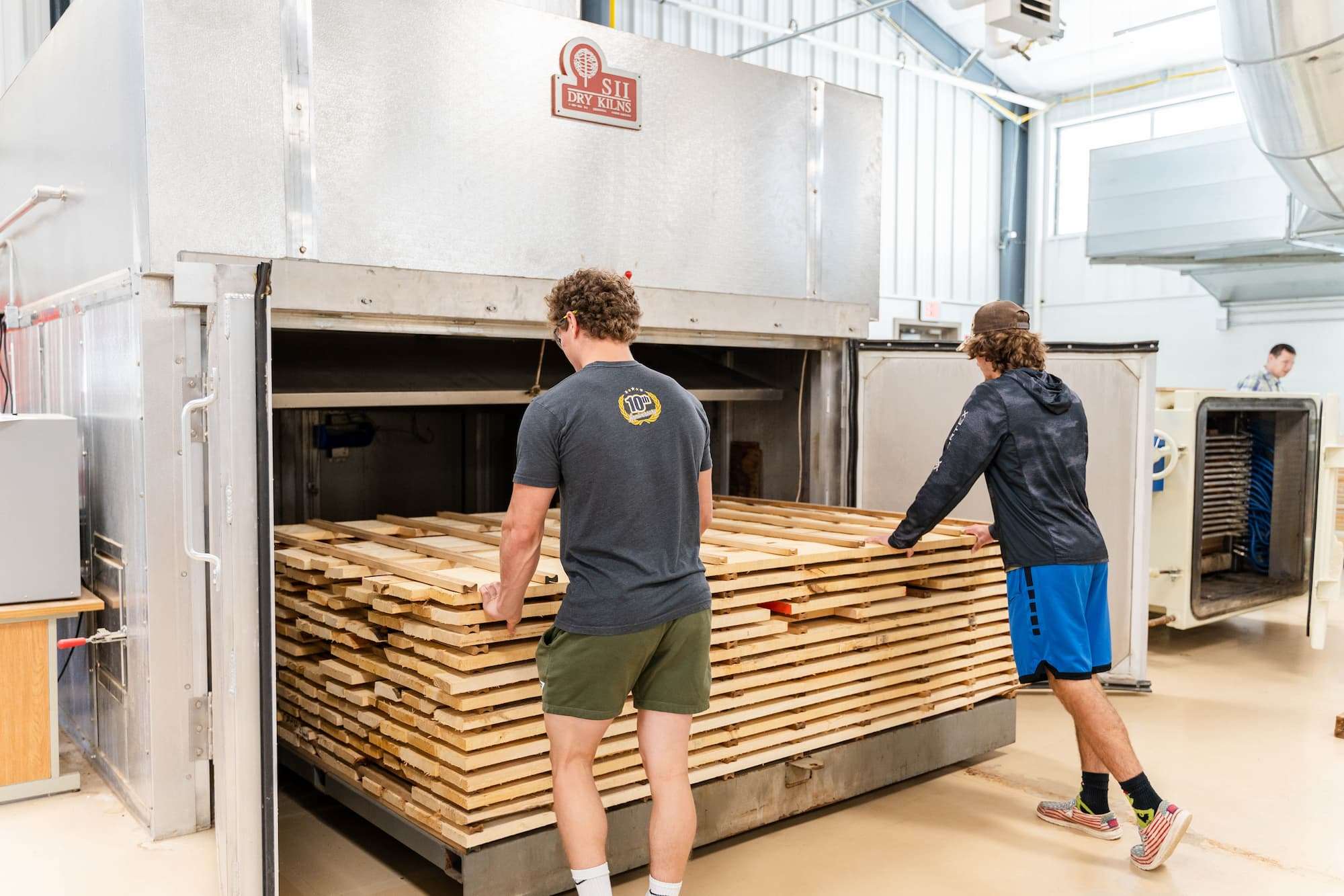 Two students push a large cart of lumber into a kiln.