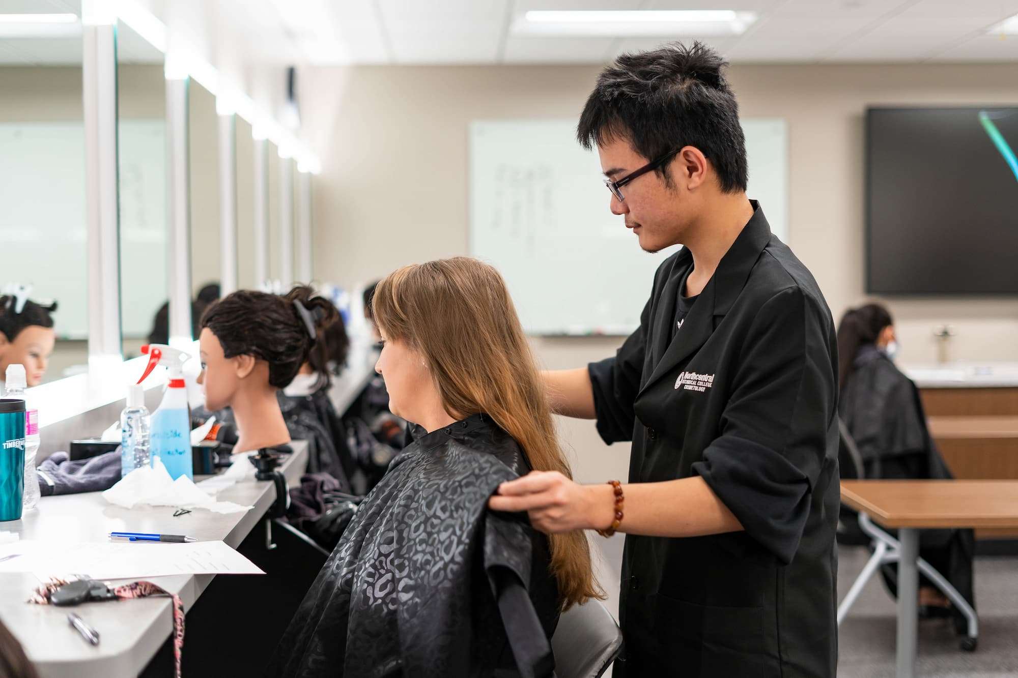 A hair stylist stands behind his client and places a cape over her.