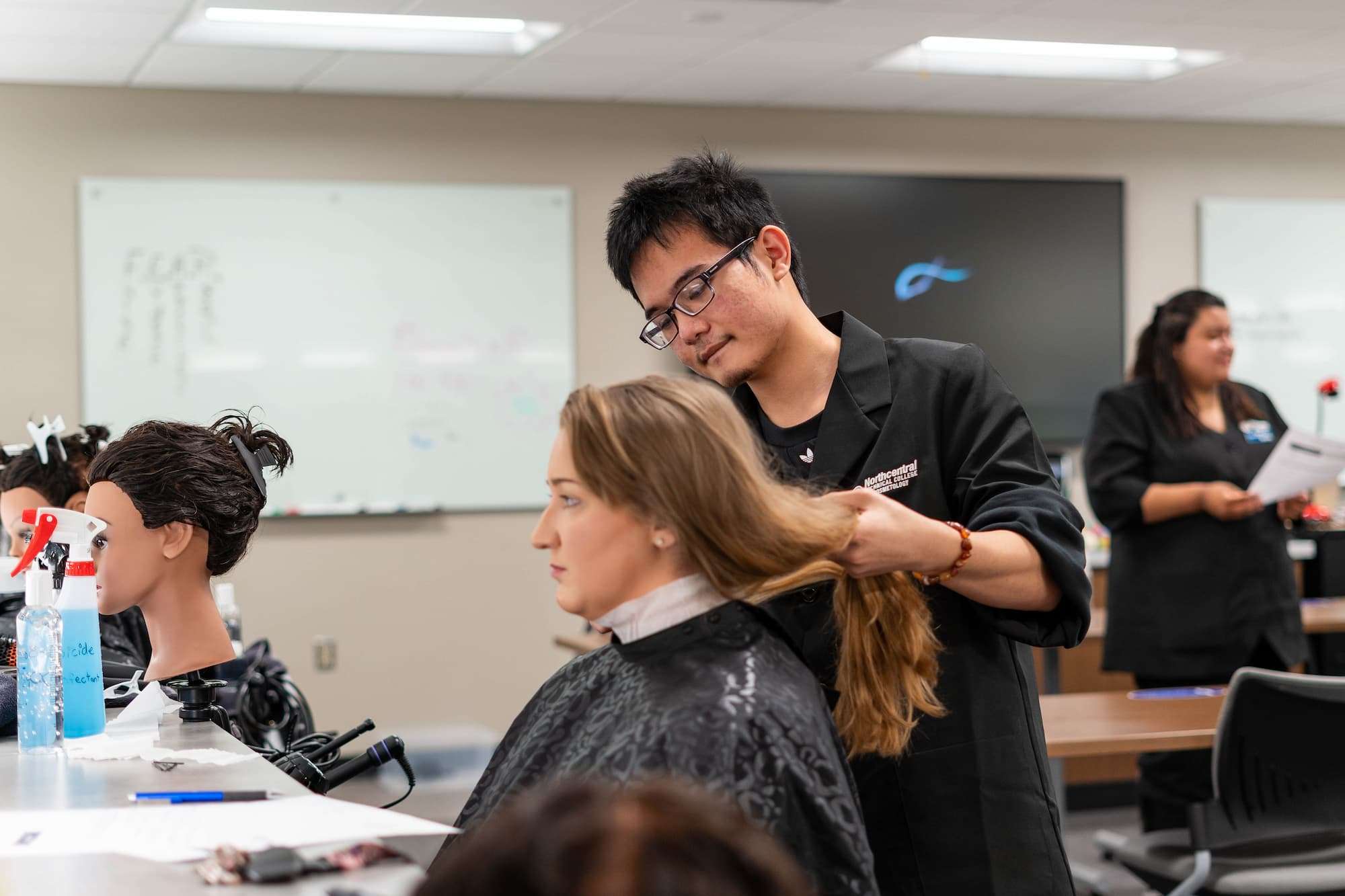 A hair stylist lifts and examines his customer's long hair.