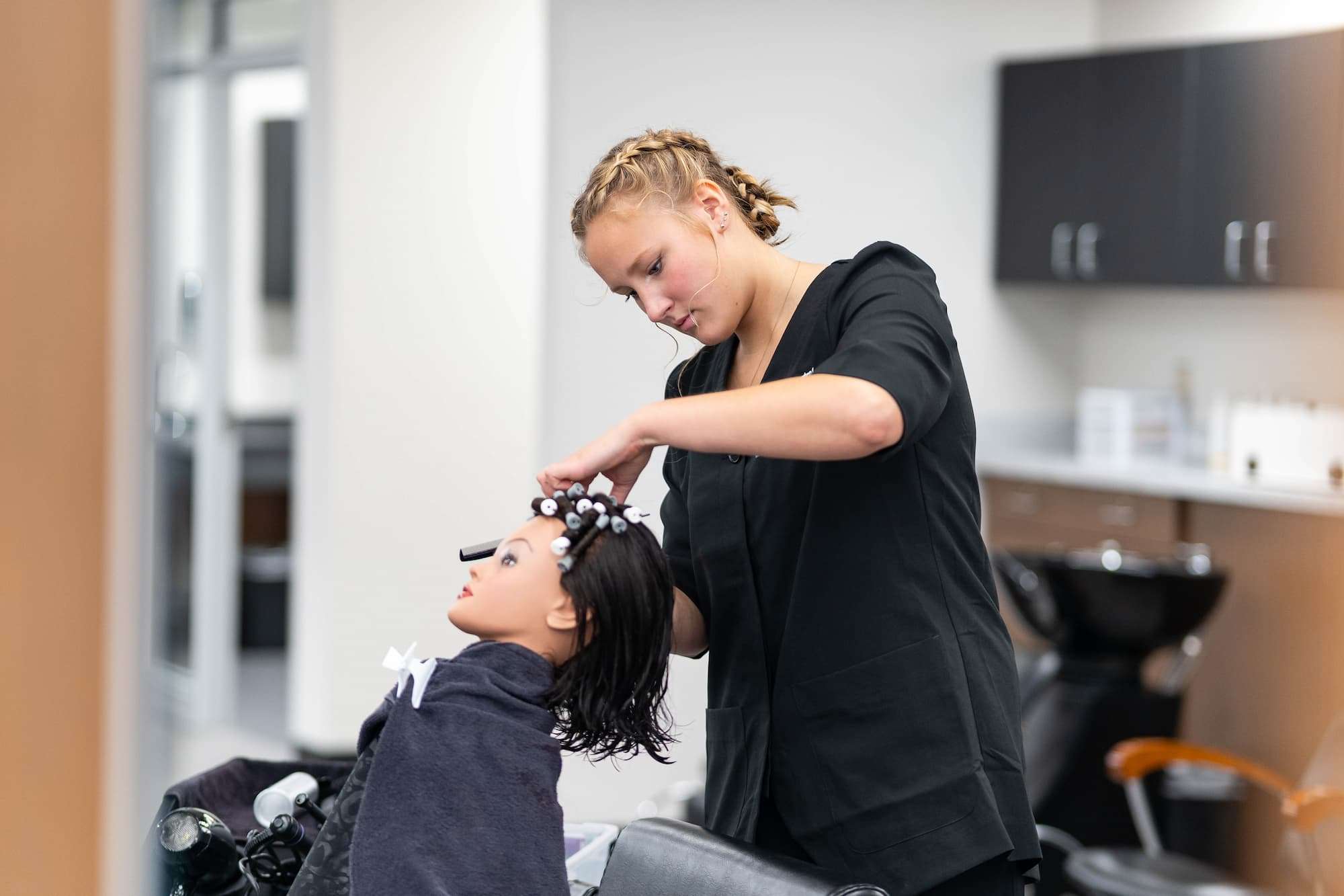 A young woman carefully places sections of a mannequin's hair into rollers.