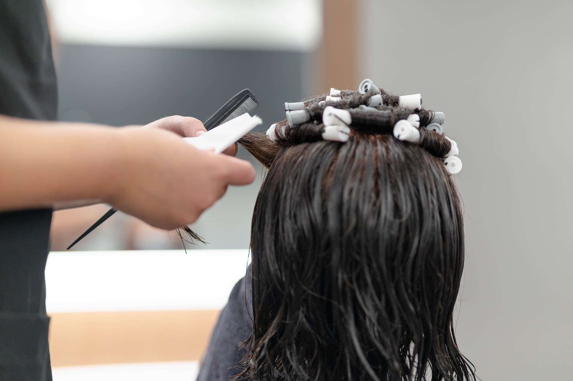 A close-up view of a student's hands as they delicately coil strands of hair into rollers.