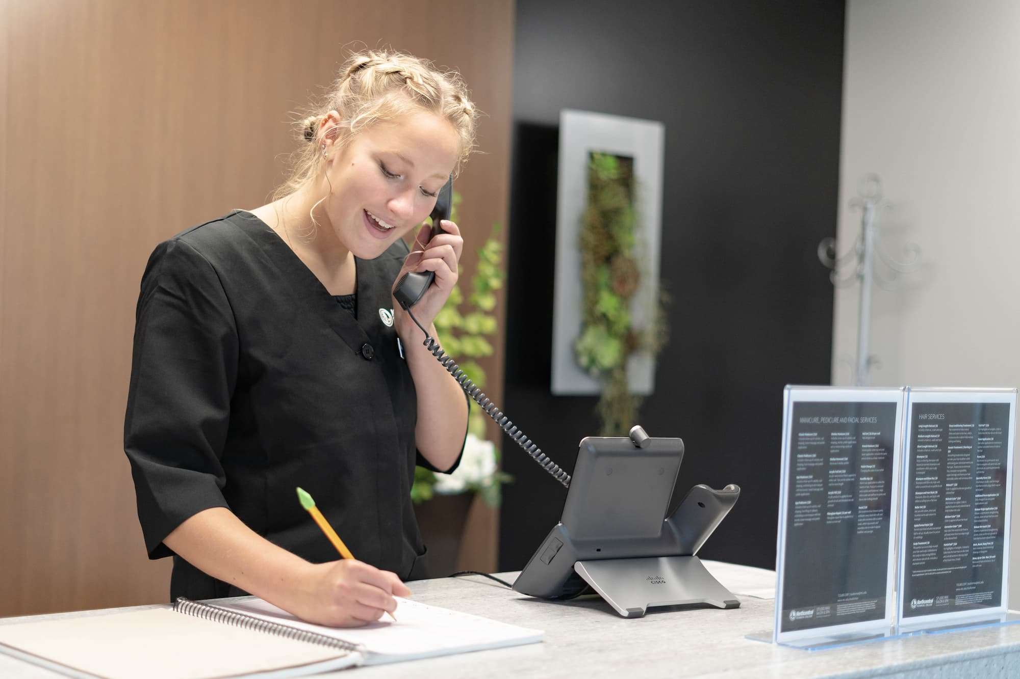 A cosmetology student taking a phone call to arrange an appointment with a customer.