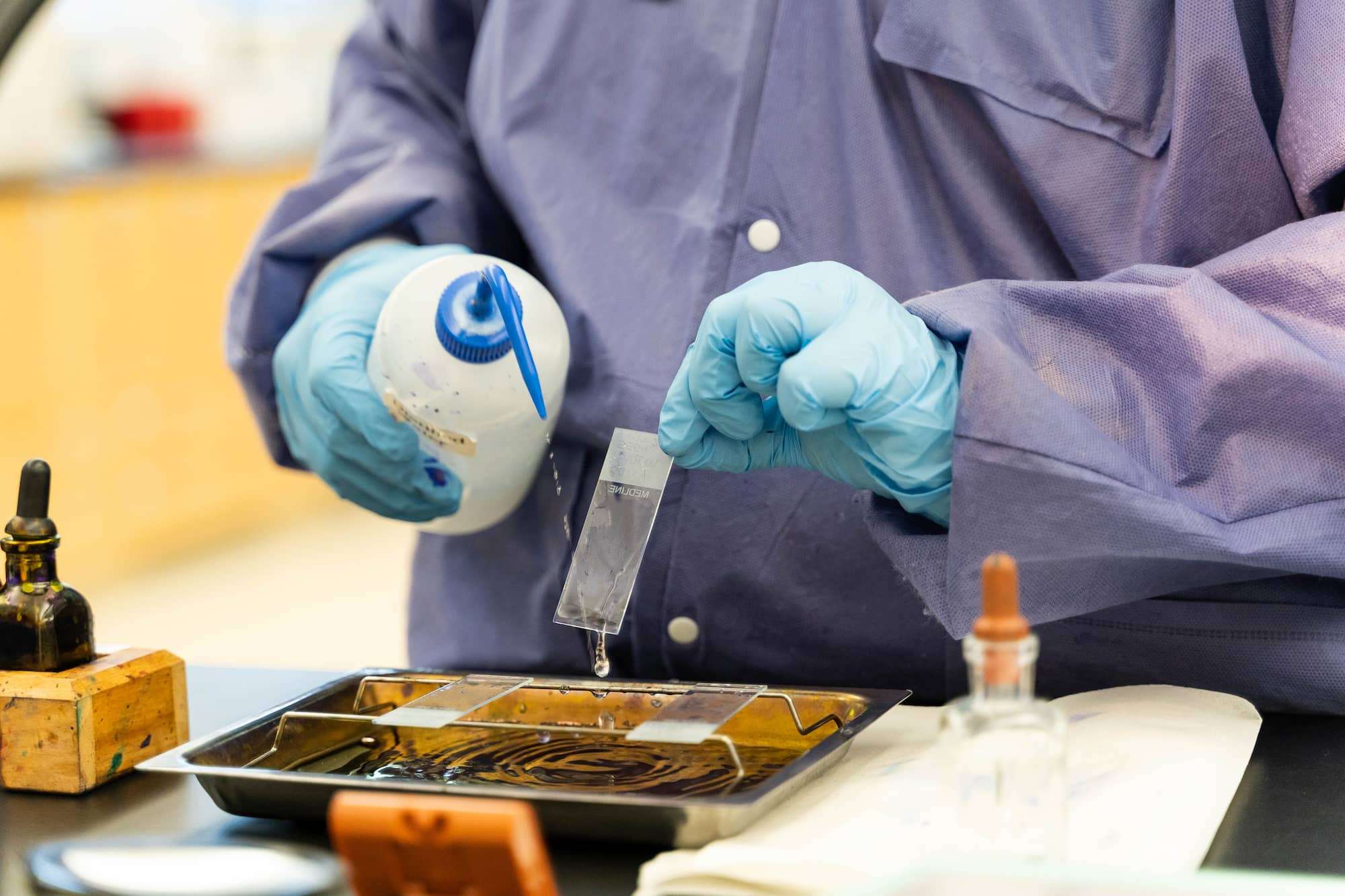 A close-up of a microscope plate being rinsed with distilled water from a squeeze bottle.