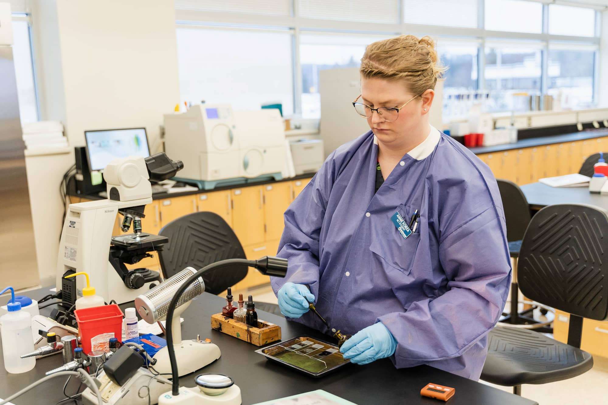 A student prepares to examine samples under a microscope by adding drops of an inky solution to three sample plates.