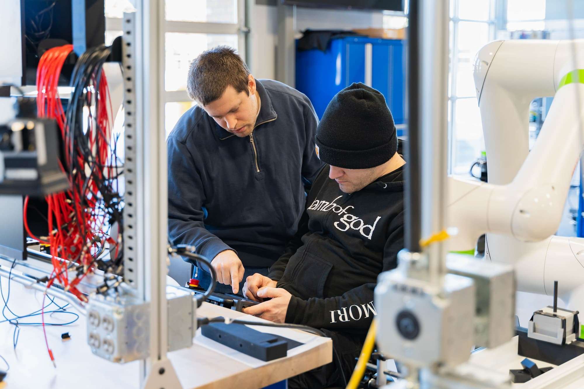 Two men huddle together, operating the interface of a manufacturing robot.