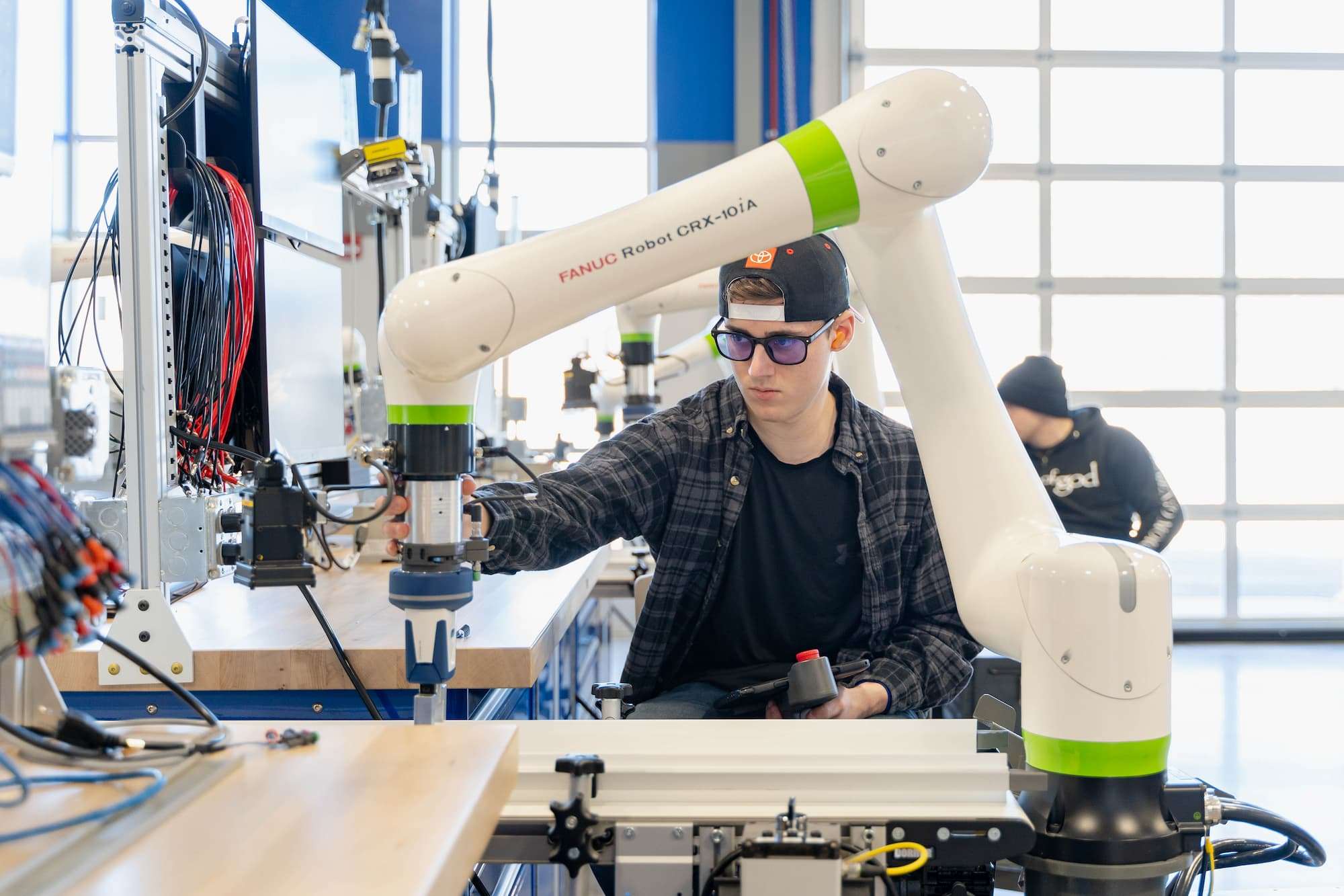 A student prepares and manually adjusts the position of a smart manufacturing robot.