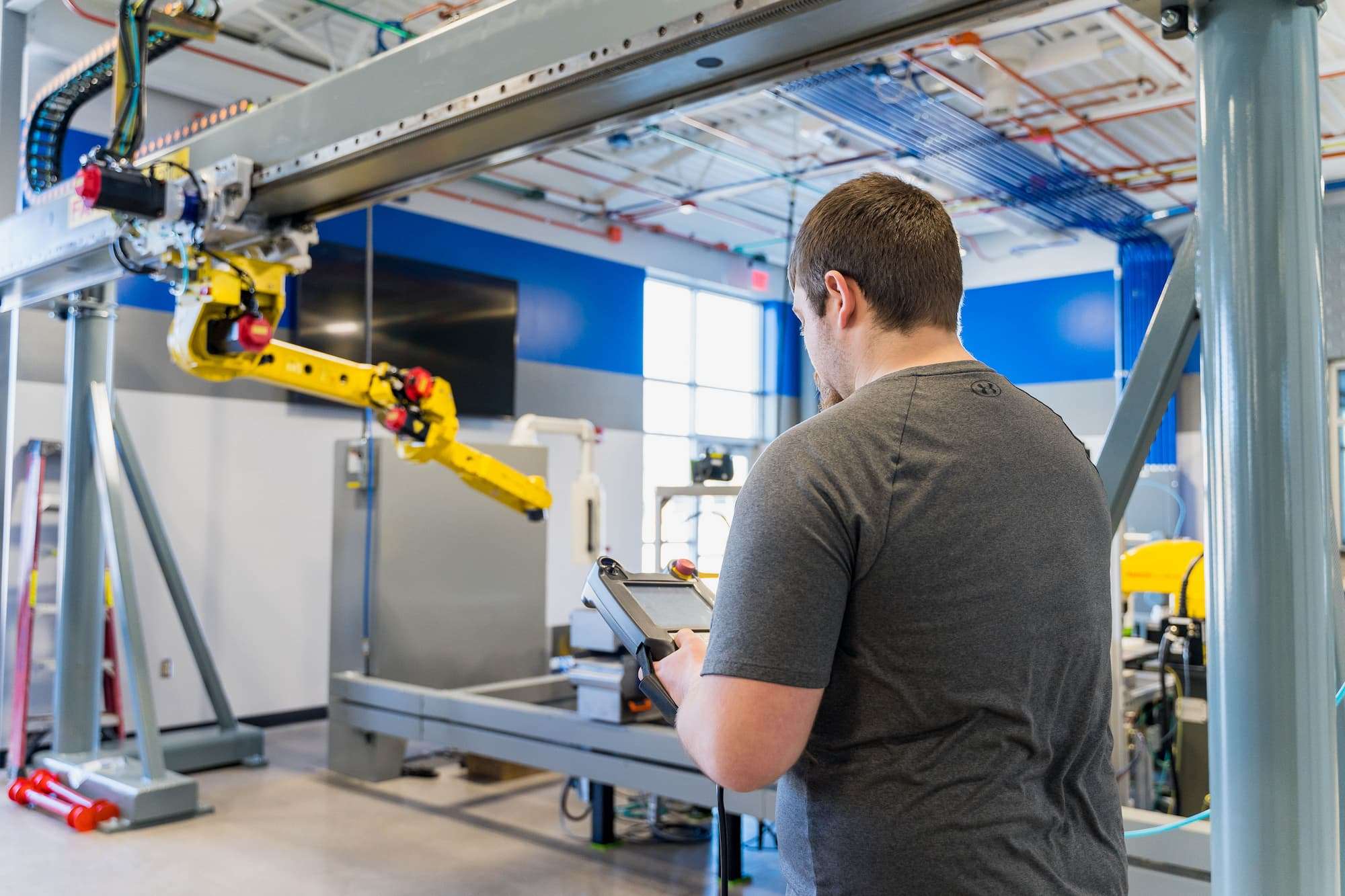 A student stands to operate a large, ceiling-mounted industrial robot.