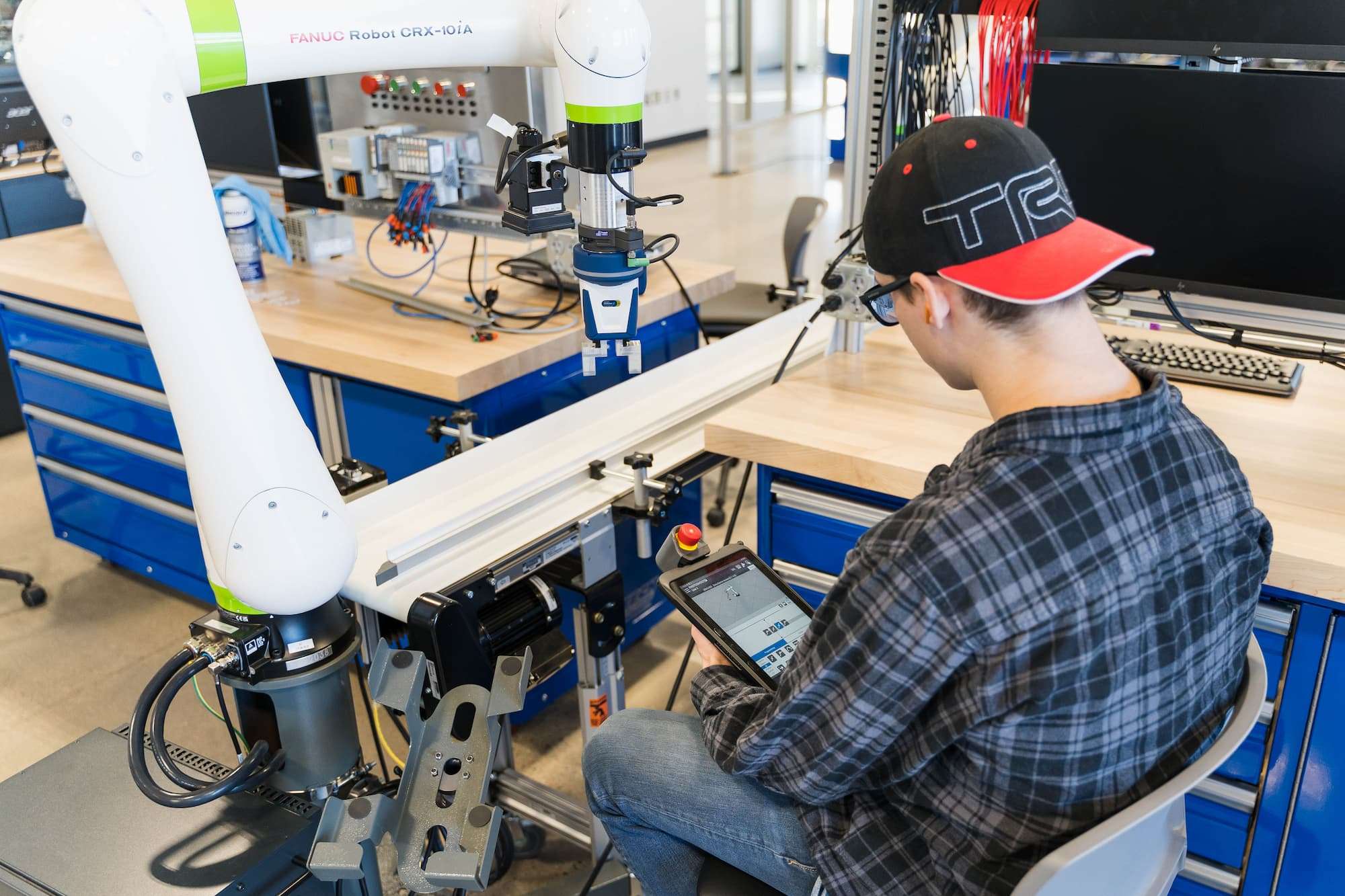 An over-the-shoulder view shows the touch screen interface that a student is manipulating to operate a robot.