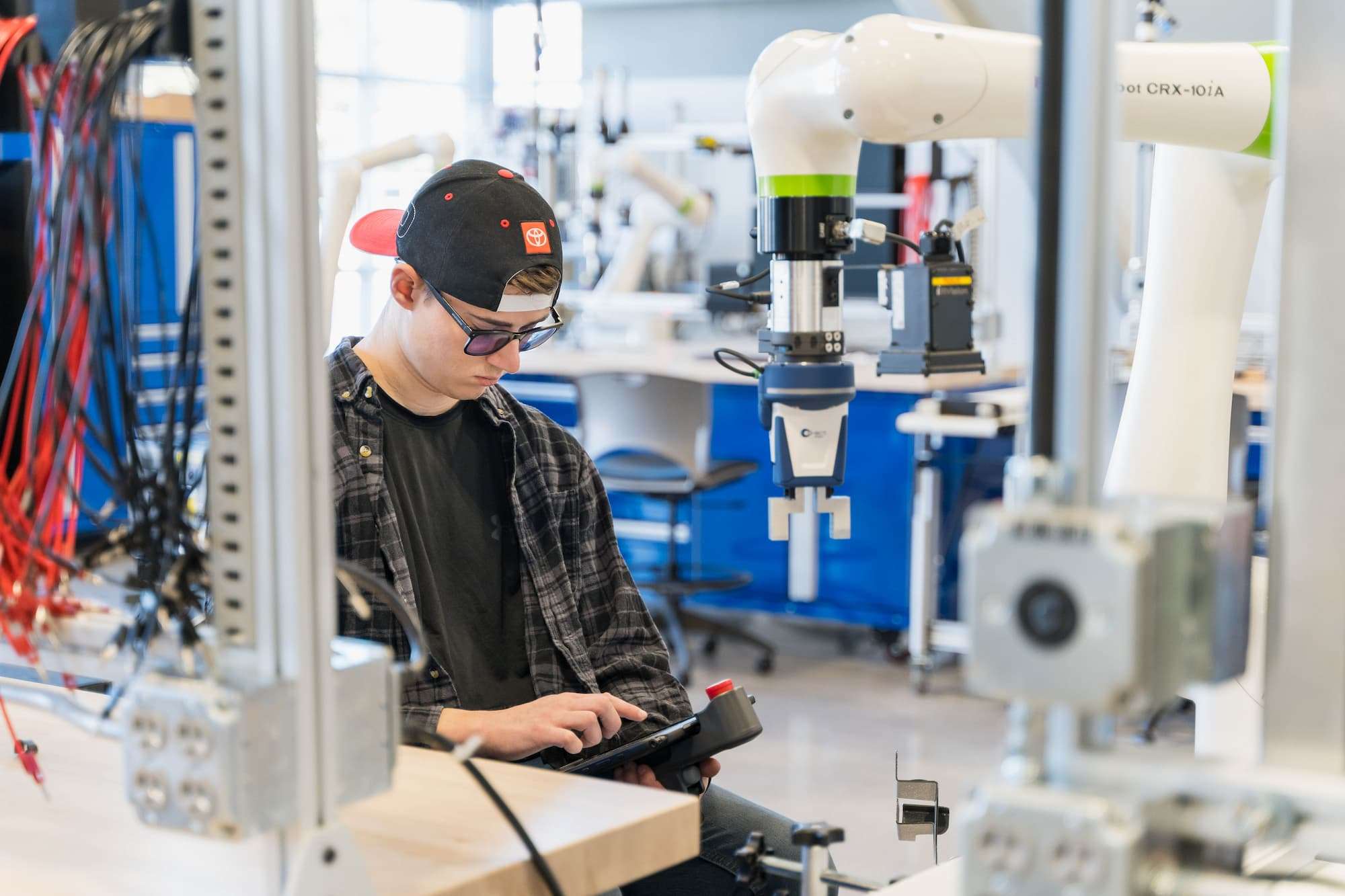 A student presses a touchscreen device to operate a robotic arm.