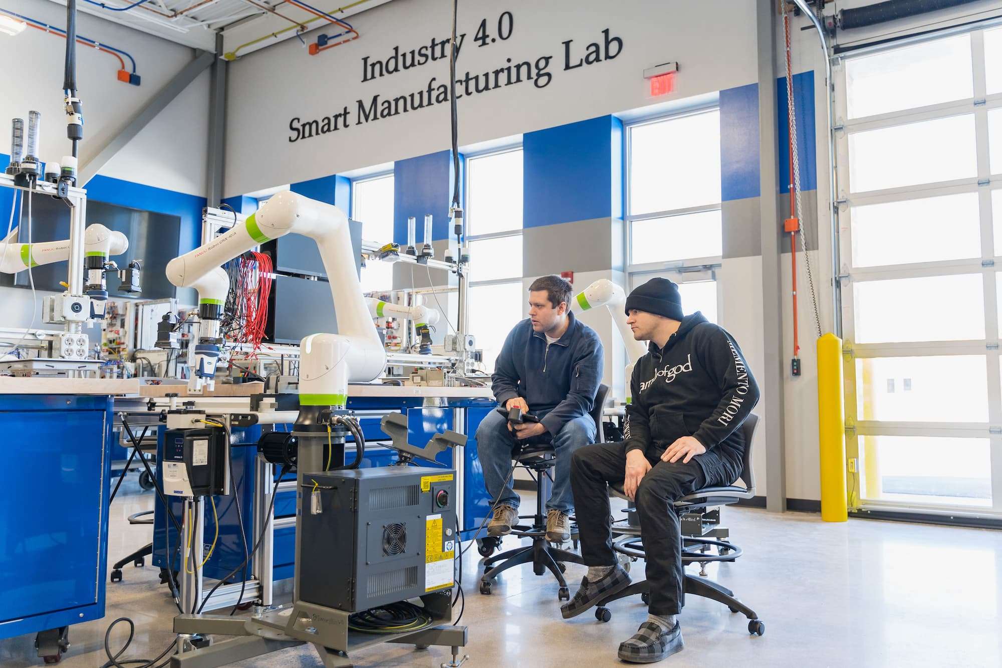 A low-angle view shows NTC's Smart Manufacturing Lab, with natural light flooding the area through high windows and exterior shutter doors.