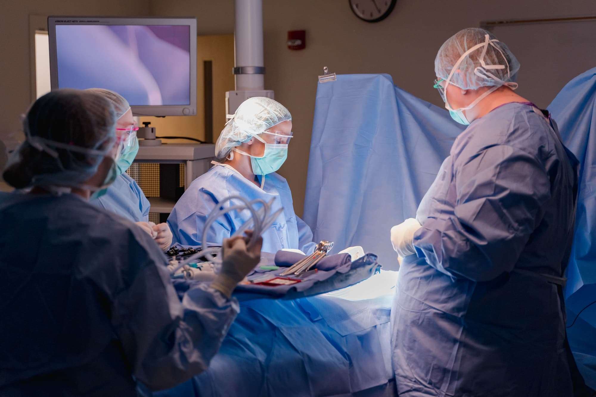 A close-up view shows two students leading the mock operation, as others hand over tools.