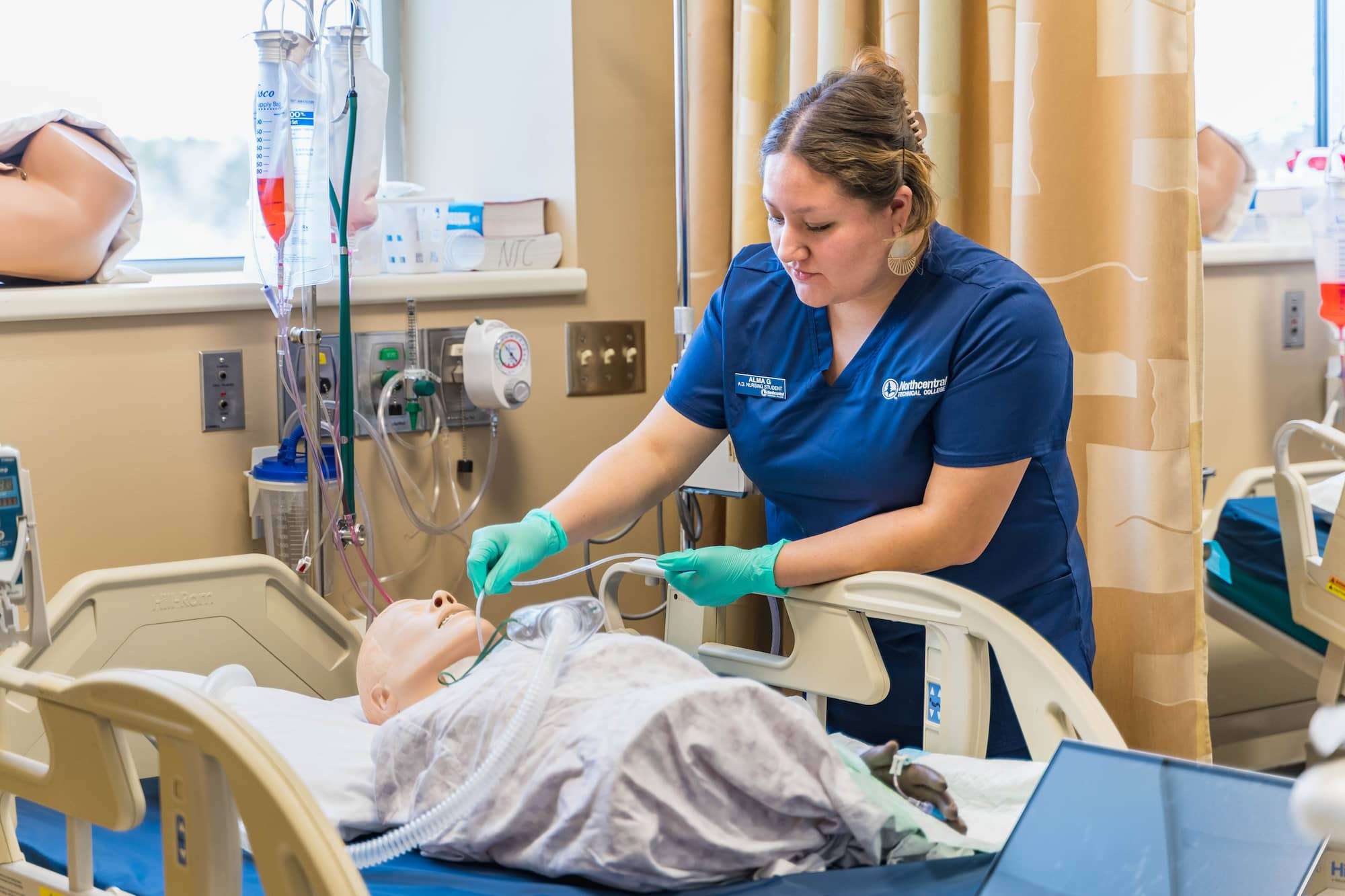 A student holds clear plastic tubing in place to a mannequin for oxygenation.