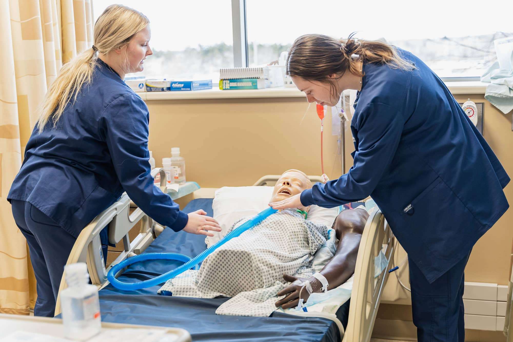 Two students check a large, blue tube that has been attached near a mannequin's throat.