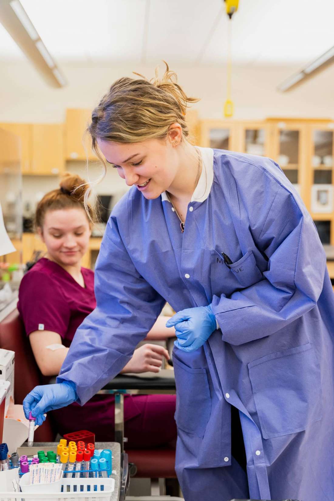 A phlebotomy student smiles while returning a phial to storage.