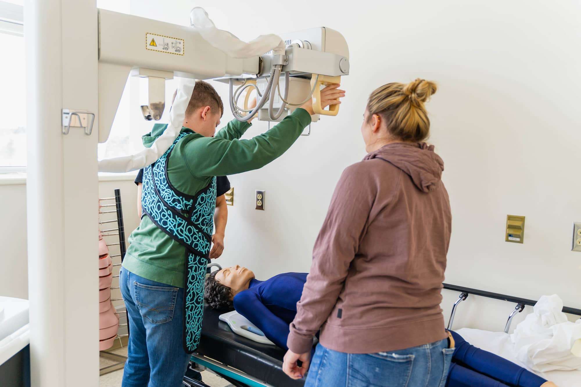 A student positions a radiography system over a mannequin.