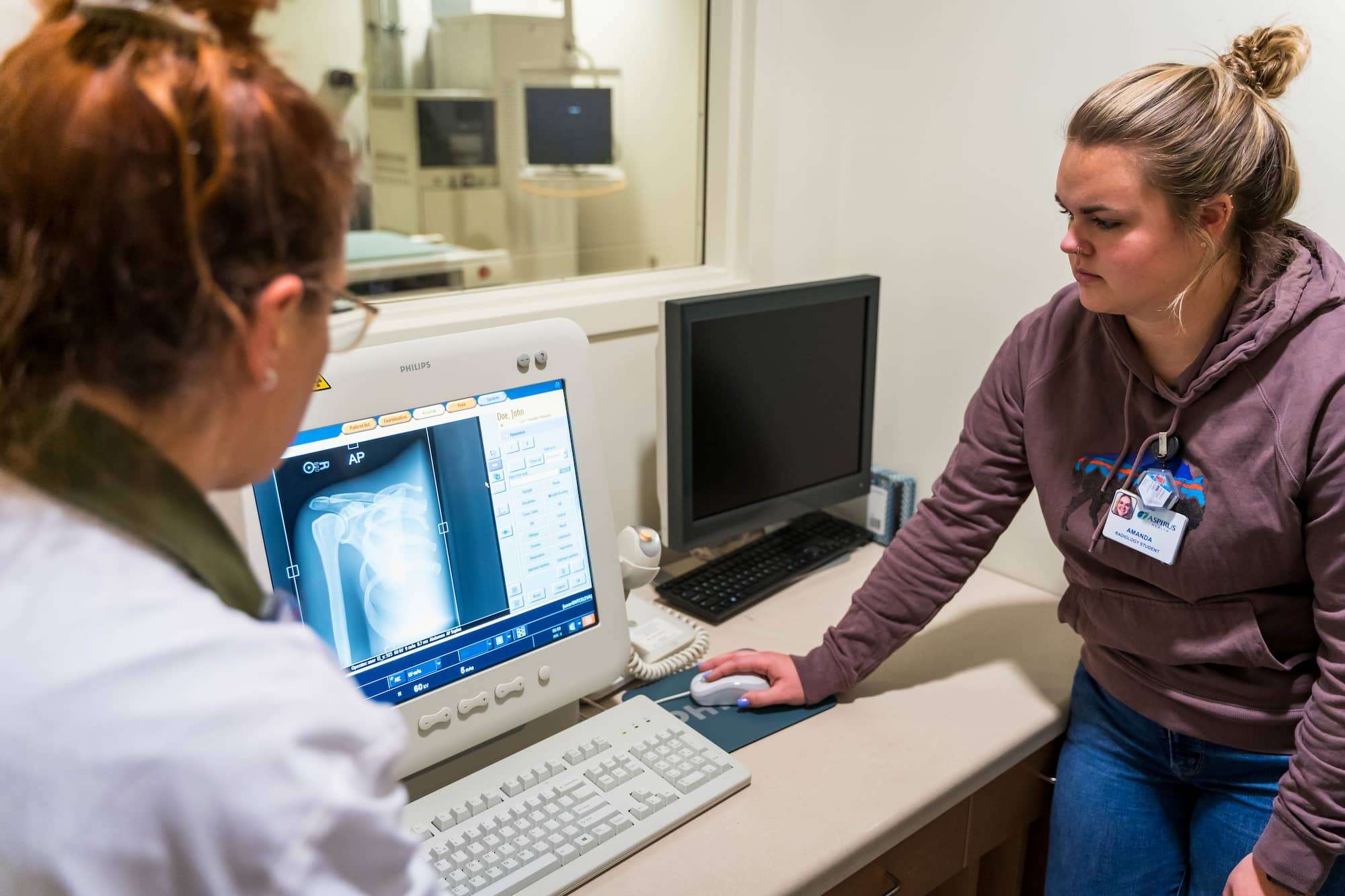 X-ray imaging of a shoulder displays on screen while a student examines with her instructor.