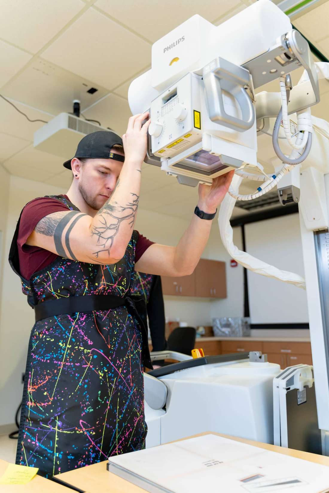 A student wearing a lead apron practices aligning the radiography system over the center of a paper target.