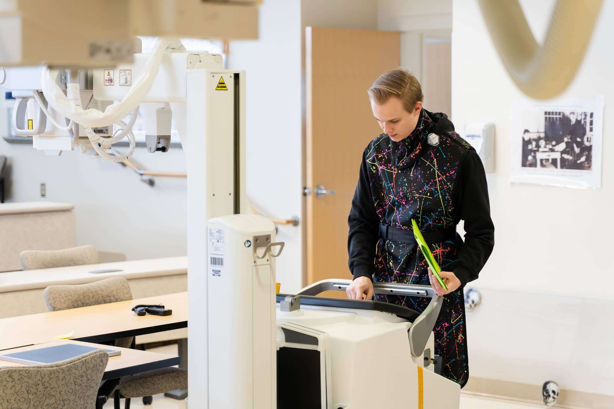 A student reviews information on an imaging computer. He's wearing a black lead apron, with a stylish pattern of thin "paint" lines in a variety of neon colors.