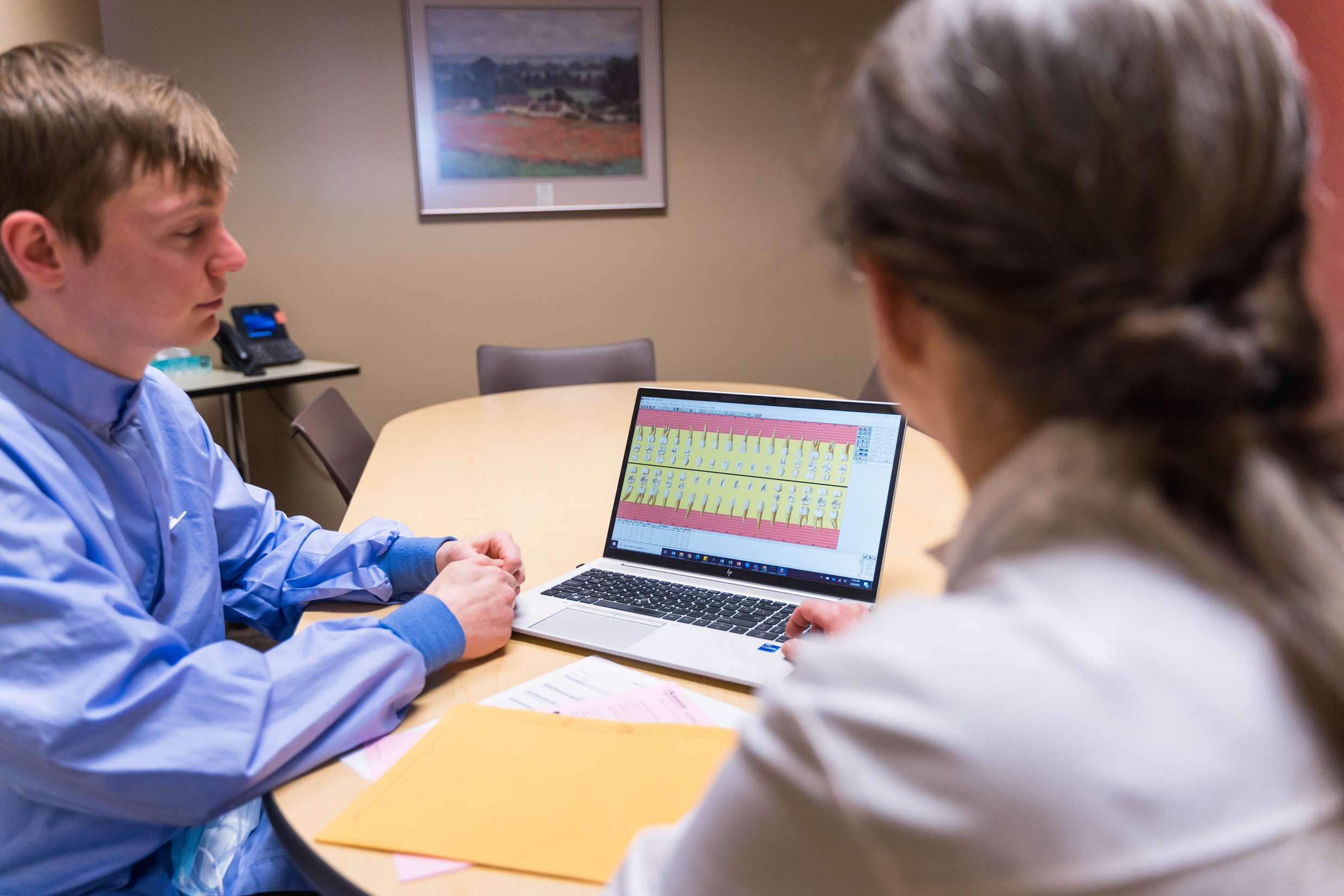 Two dentists are looking over a patients dental records on a laptop inside of a meeting room.