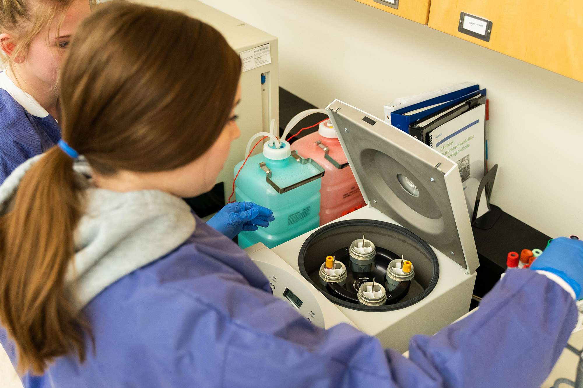 An overhead view of a Medical Assistant placing blood samples into a centrifuge machine.