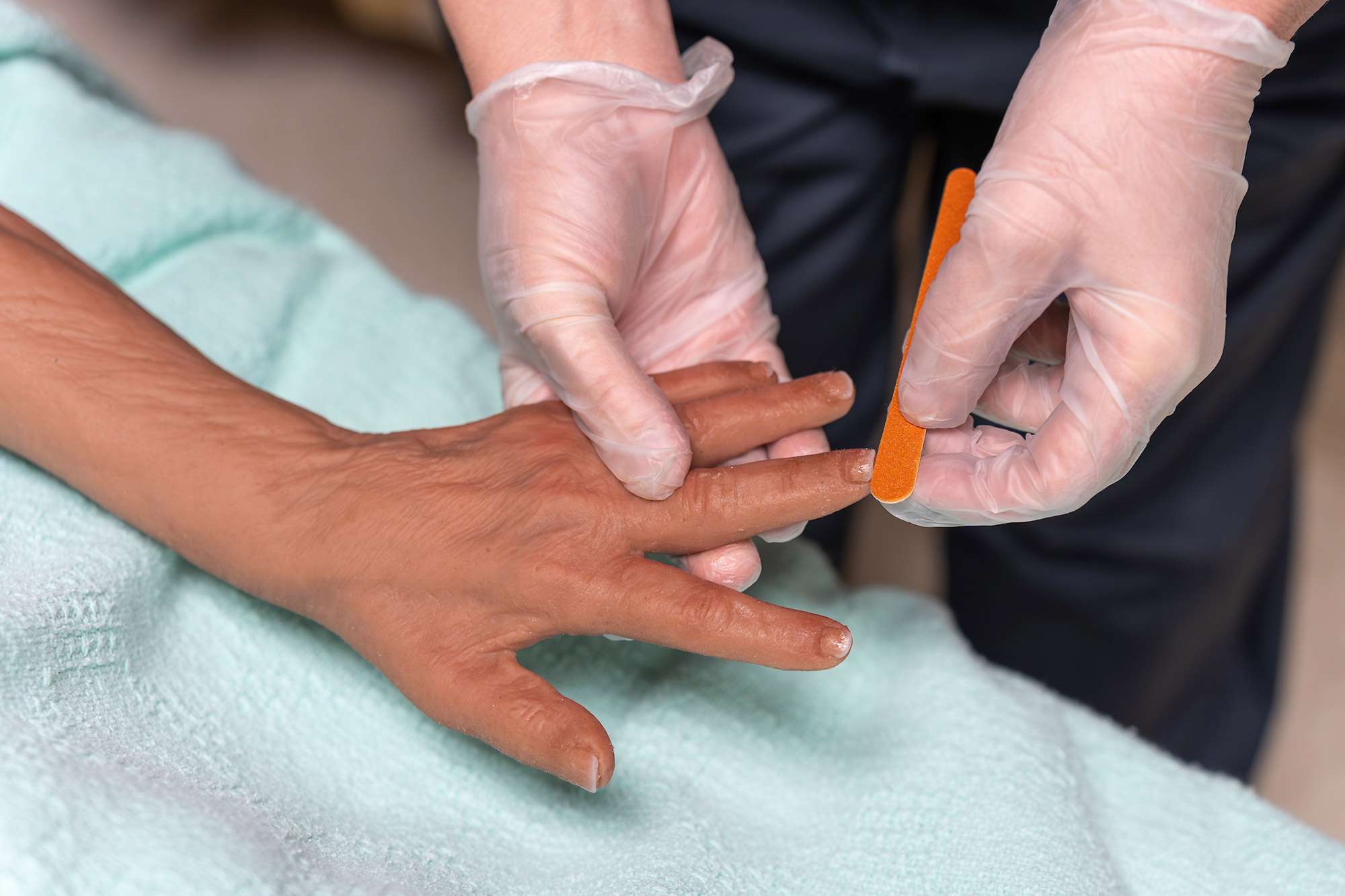 A certified nursing assistant uses a nail filer on the hand of a mannequin.