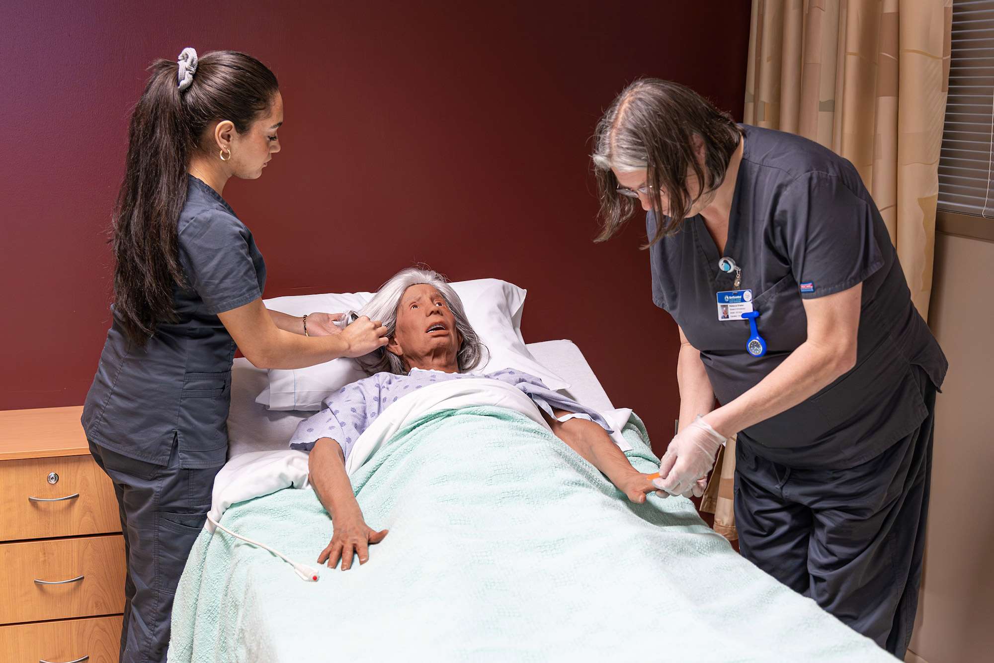 Two Certified Nursing Assistants use an elderly mannequin as practice for brushing hair and teeth.