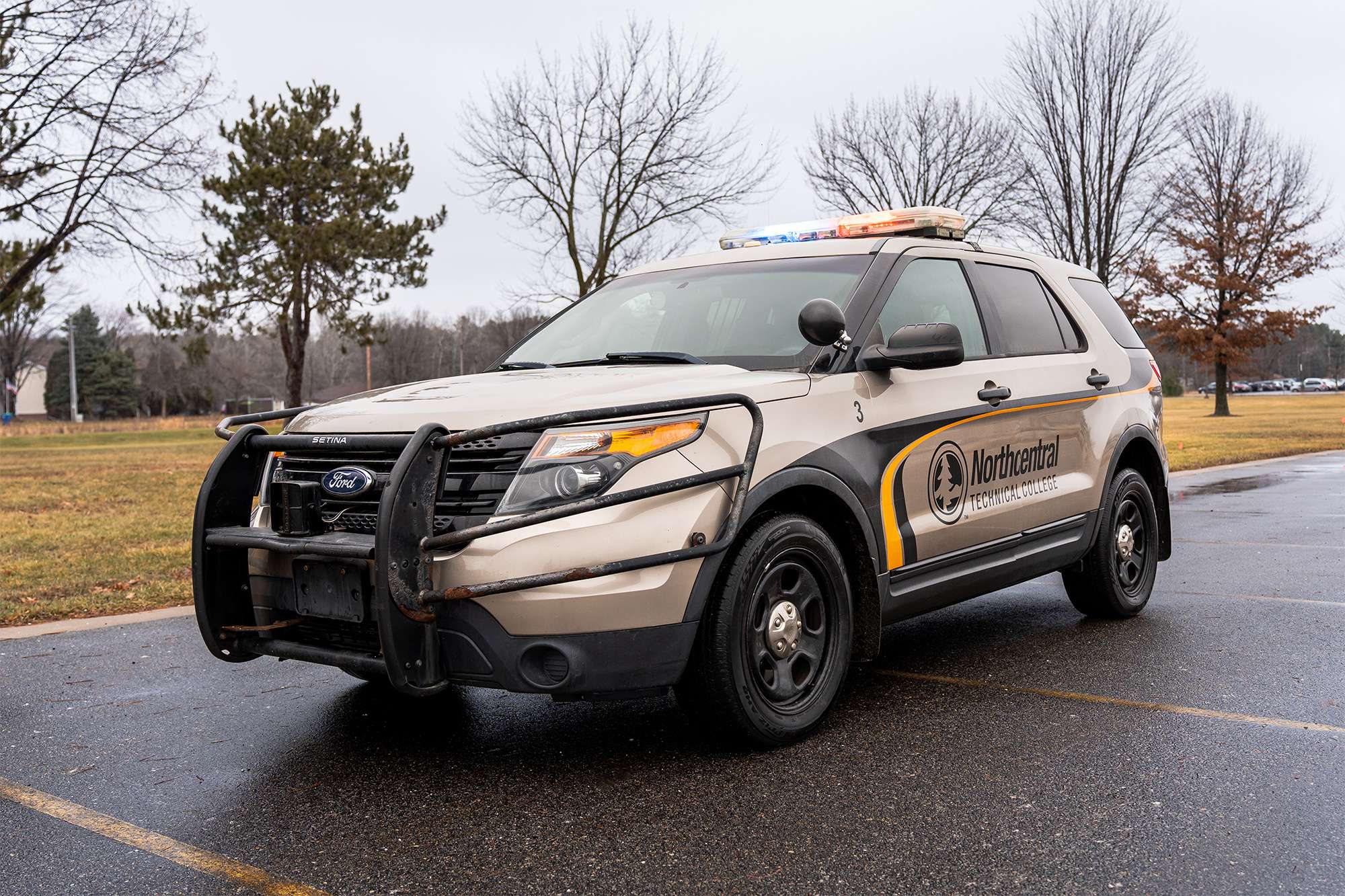 A Northcentral Technical College law enforcement training vehicle with emergency lights on is parked in a lot.