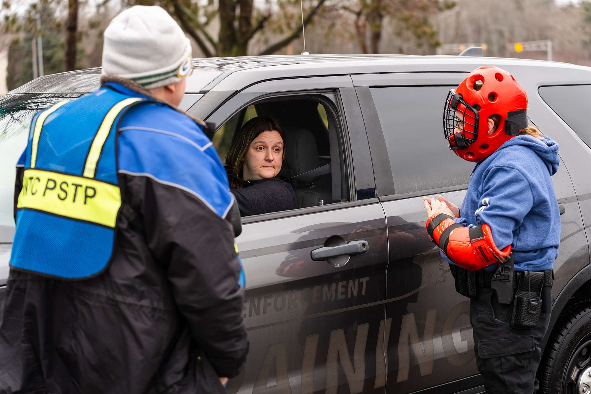 A trainee in red protective gear interacts with a driver during a law enforcement training exercise.