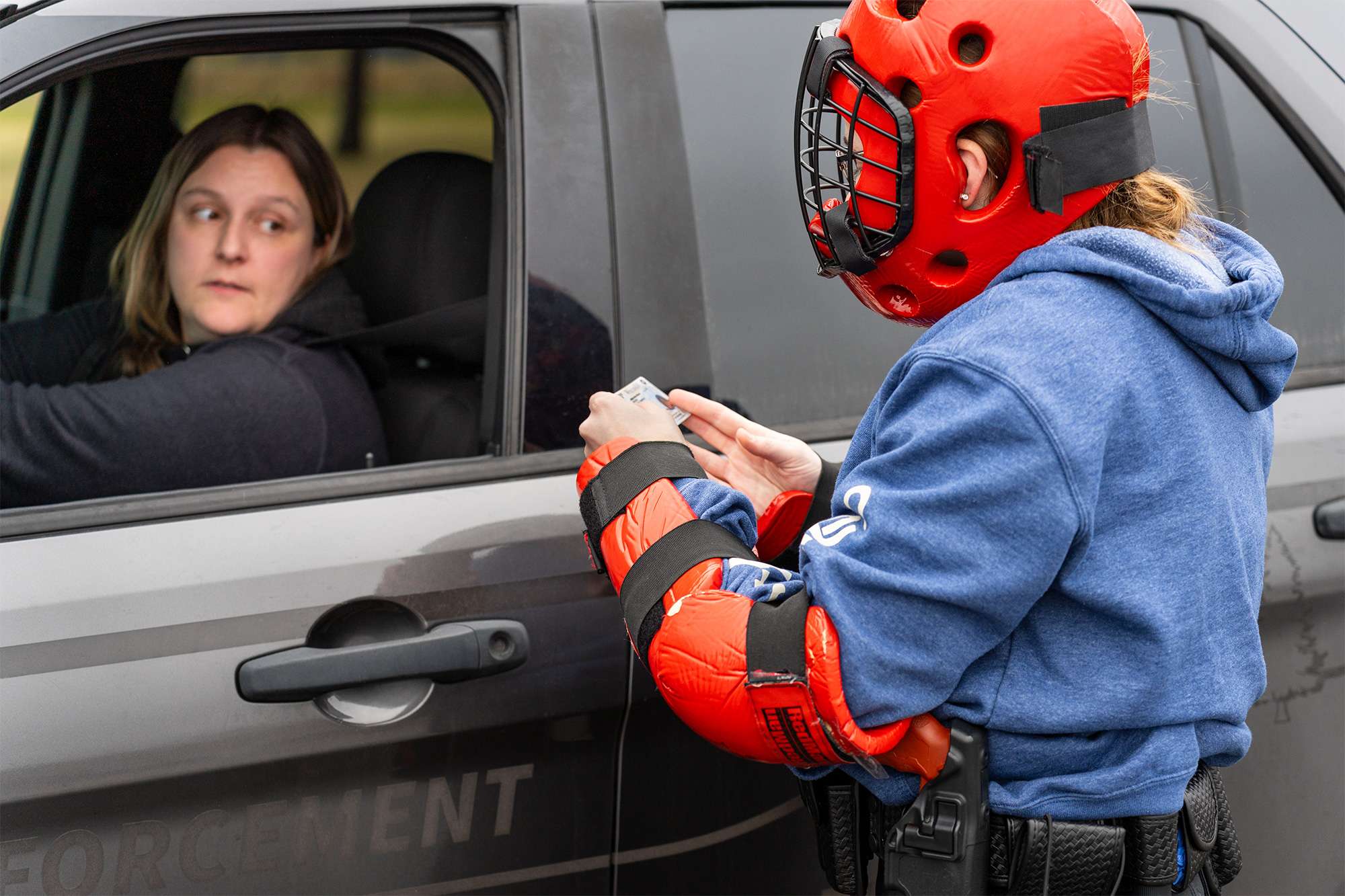 A trainee in red protective gear checks a driver's ID during a law enforcement training exercise.