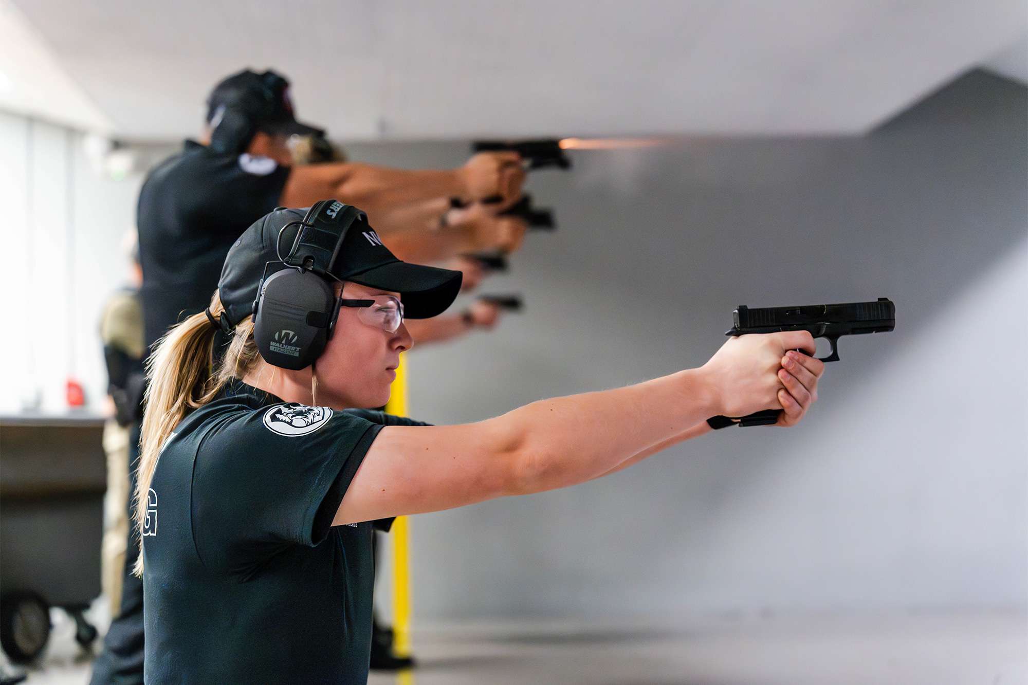 A police academy trainee in protective gear fires a handgun at a shooting range during a firearms training session.