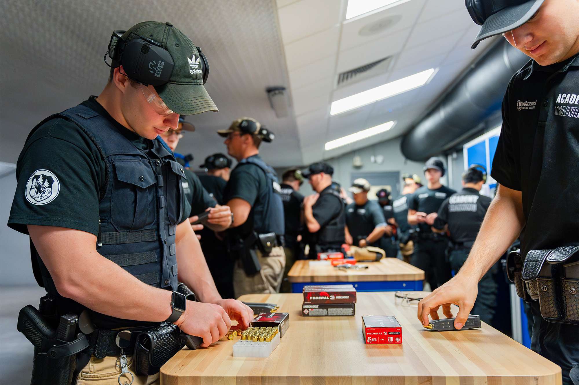 Police academy trainees in tactical gear load ammunition into magazines during a firearms training session.