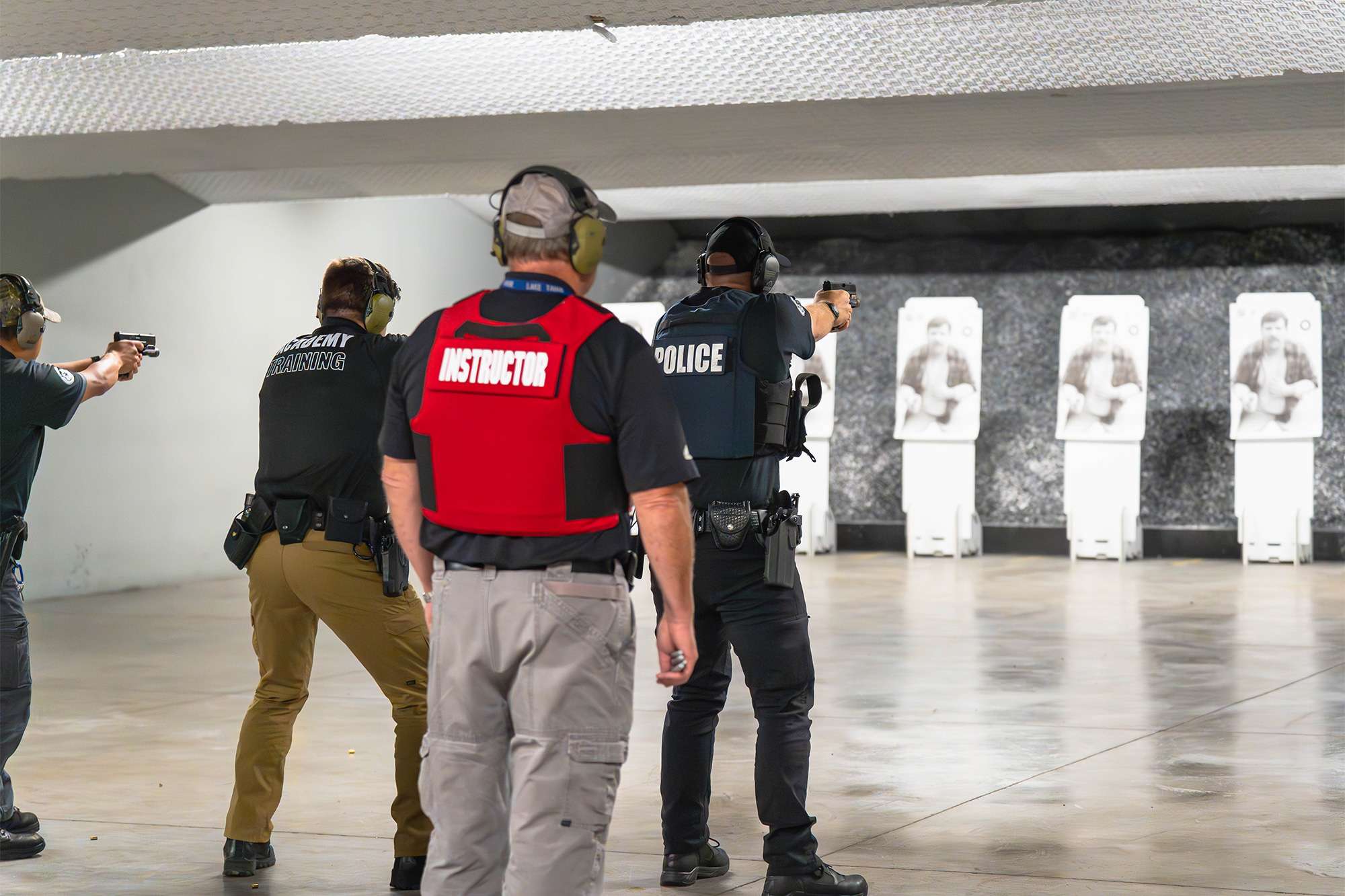A firearms instructor observes police academy trainees practicing shooting at a range, aiming at targets.